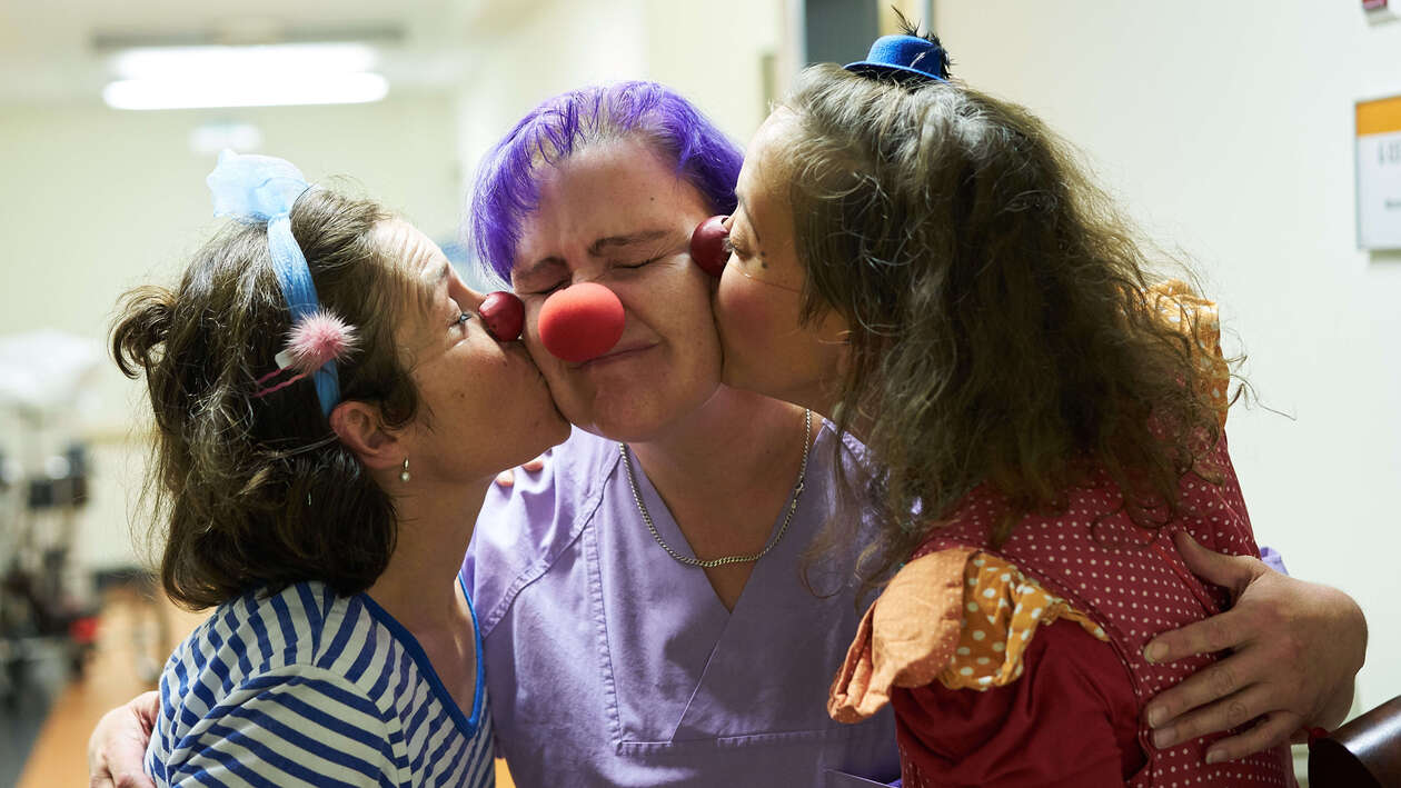 Zwei Klinikclowns geben einer Pflegekraft von jeder seite einen kuss auf die wange 