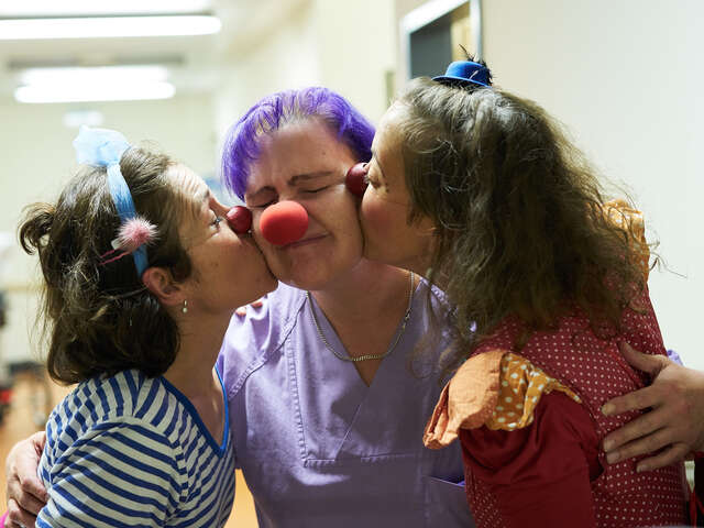 Zwei Klinikclowns geben einer Pflegekraft von jeder seite einen kuss auf die wange 