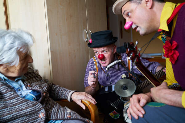 zwei männliche Clowns knien vor einer älteren Dame und erzählen ihr etwas