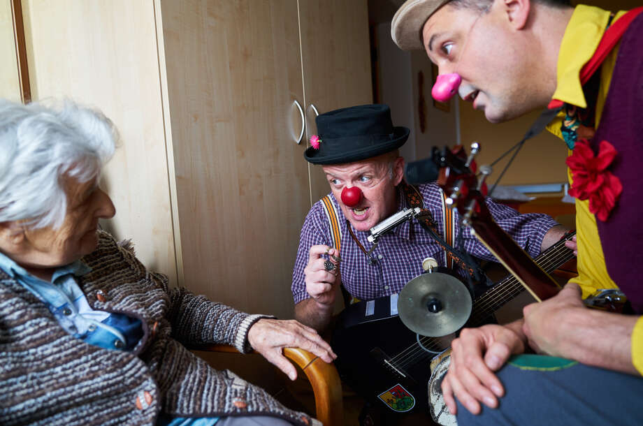 zwei männliche Clowns knien vor einer älteren Dame und erzählen ihr etwas