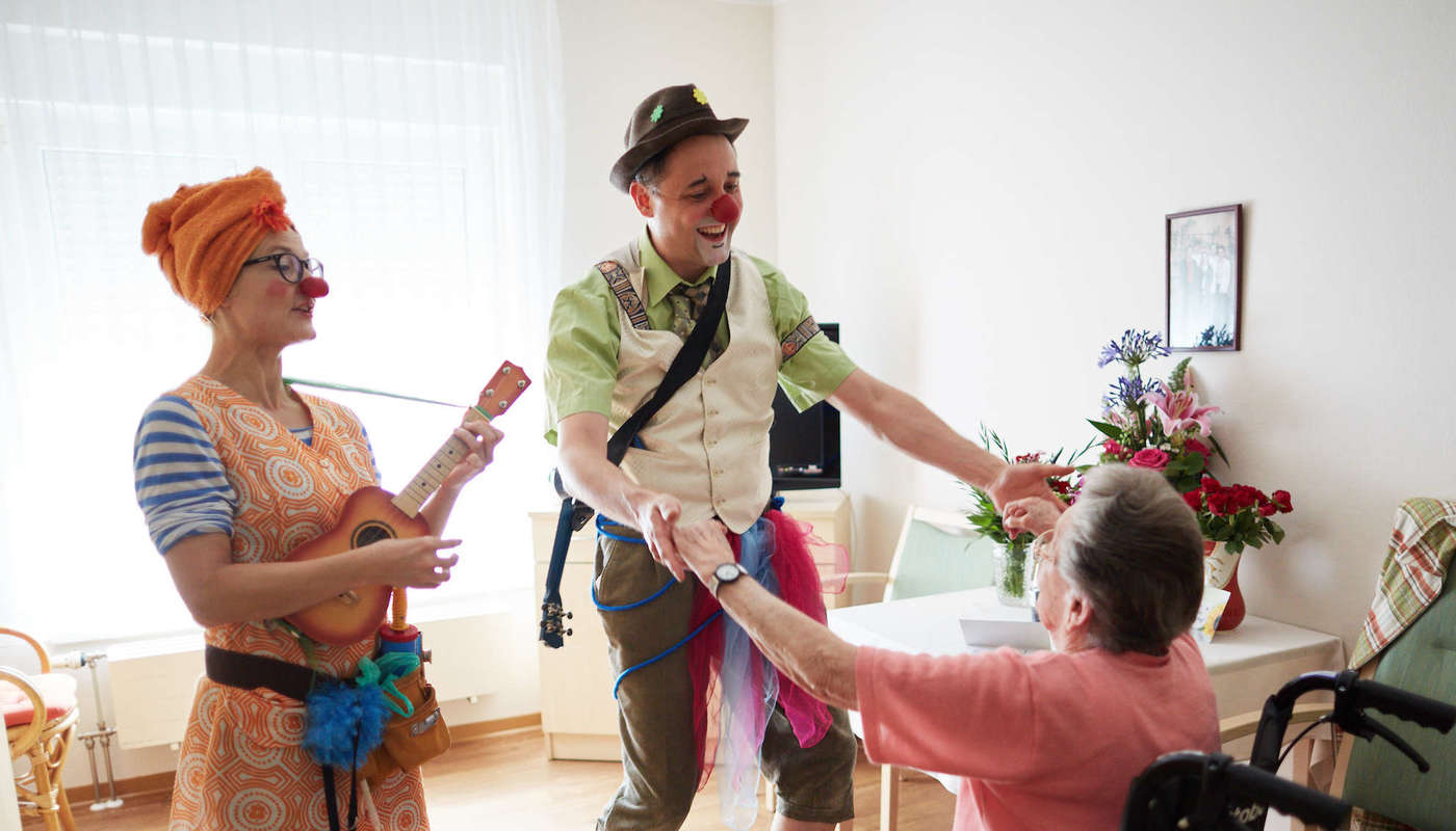 Zwei Clowns besuchen eine ältere Dame auf ihrem Zimmer im Pflegeheim