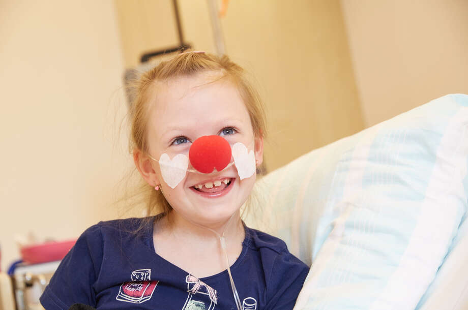 Ein Mädchen sitzt lächelt mit einer roten Nase in ihrem Krankenhausbett
