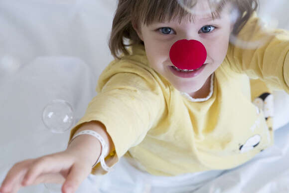 Ein Kind mit einer roten Nase auf, will von seinem Krakenbett nach denn Seifenblasen greifen 