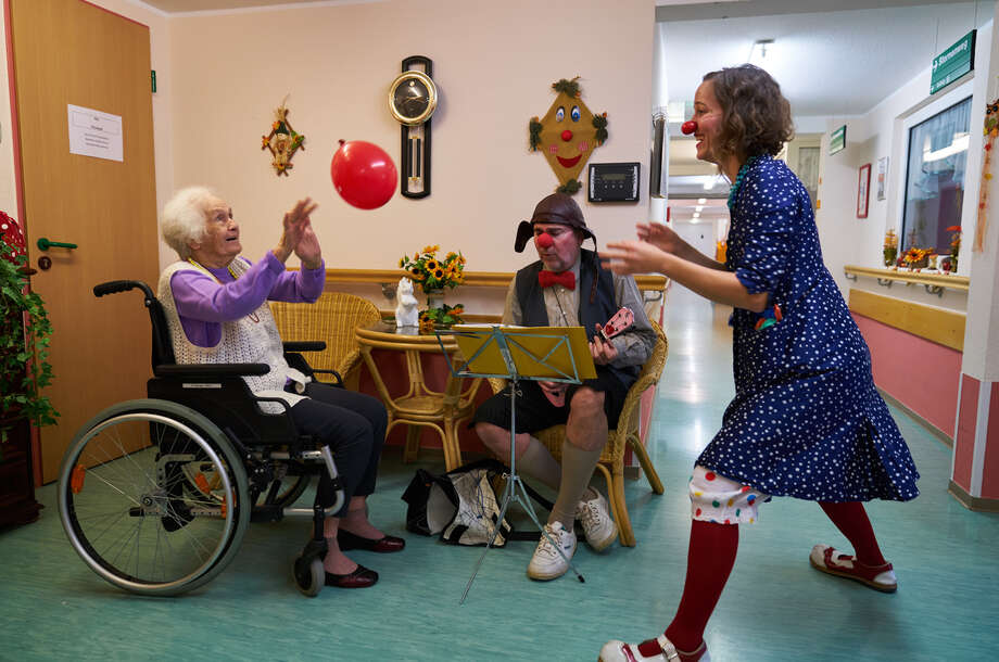 Ein Clown und ein Seniore spielen zusammen mit einem Luftballon in einem Seniorenheim