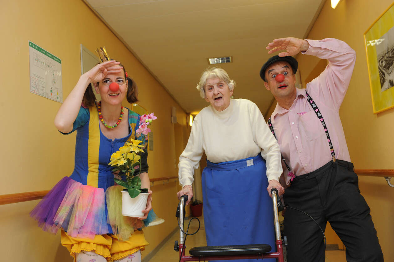 zwei Clowns zusammen mit einer älteren Dame mit Rollator schauen suchend in die Ferne 