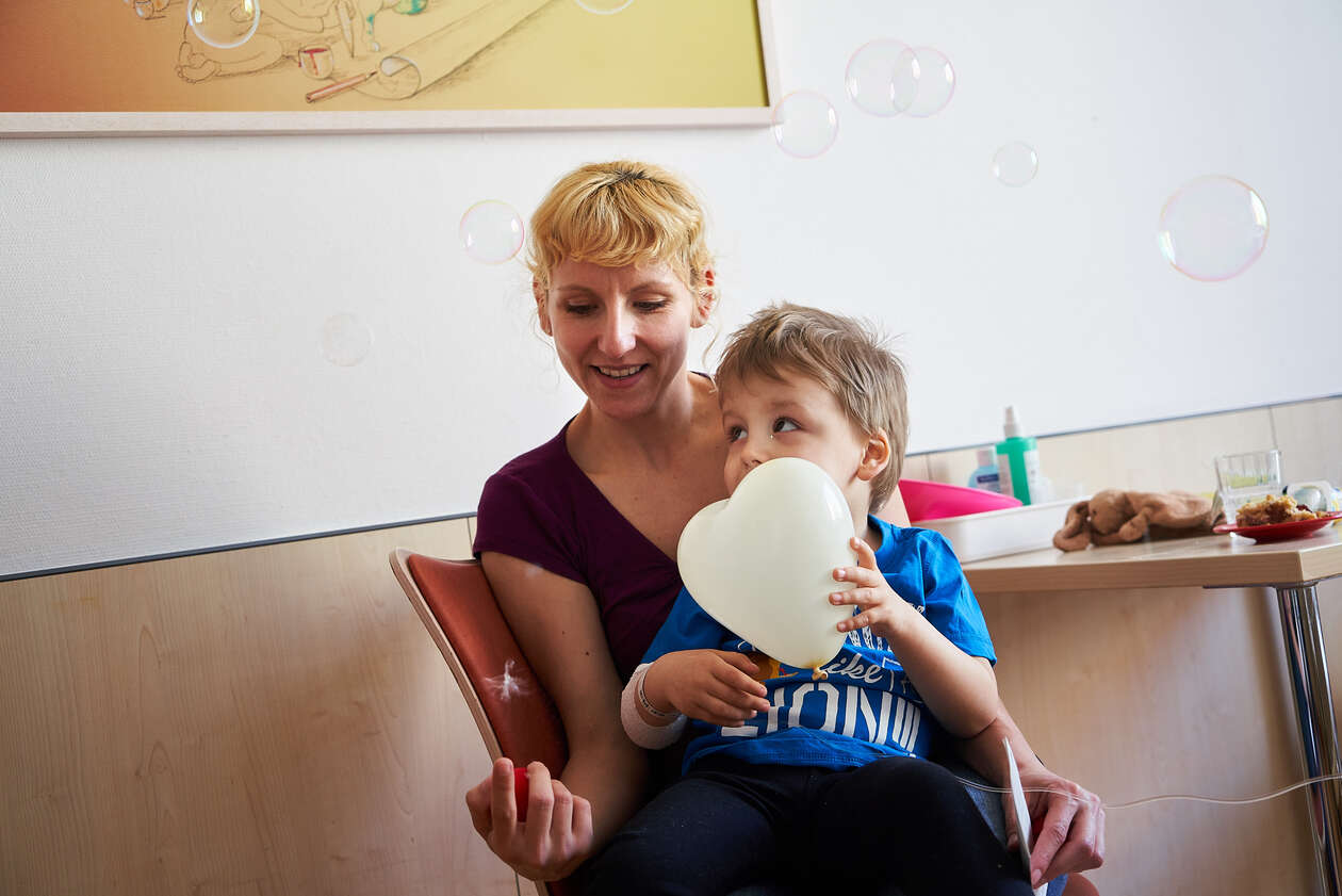 Ein kleiner Junge sitzt auf dem Schoß seiner Mutter und hält einen Herz-Luftballon in der Hand. 