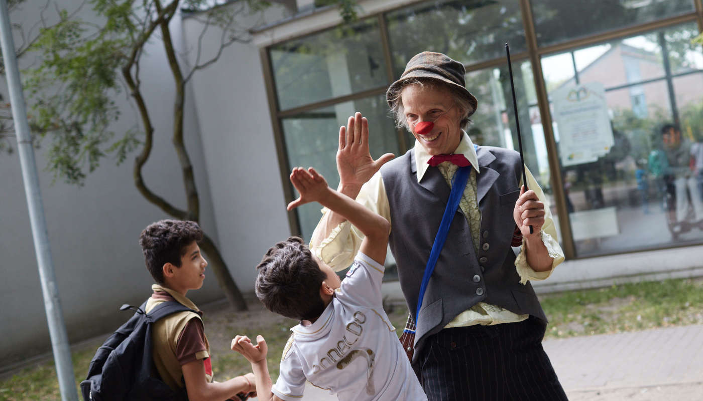 Der Clown Filou gibt einem Jungen in einem Flüchtlingheim einen Handschlag 