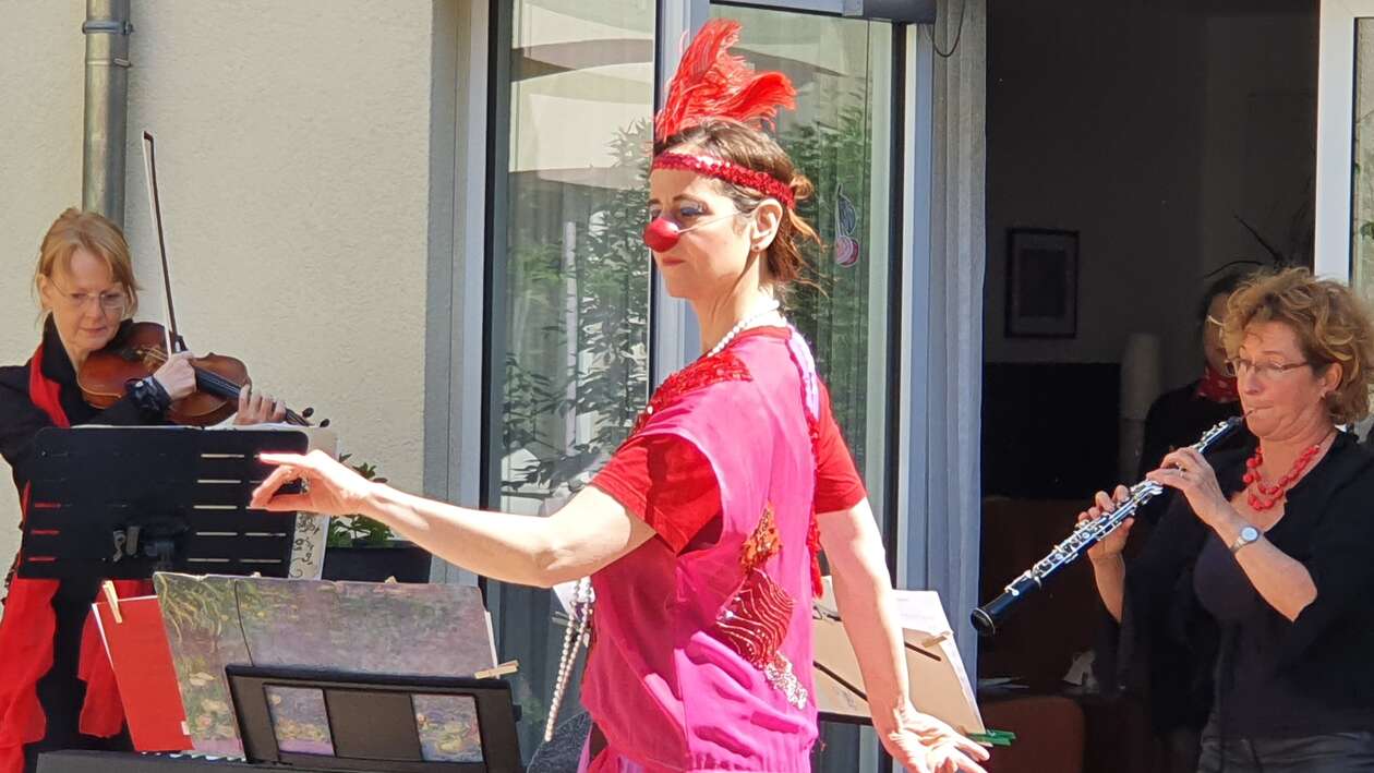 Rote Nasen Klinikclown Emma Dilemma ist mit roter Nase und Pailettenstirnband gekleidet. Im Hintergrund die Musikerinnen Gudrun Vogler an der Oboe und Anne Katrin Seidel an der Violine. 