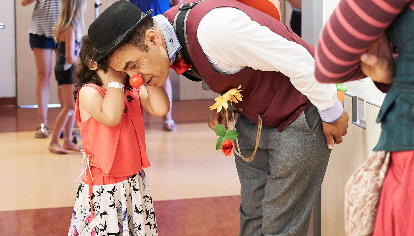 Mädchen flüstert einem Clown etwas ins Ohr.