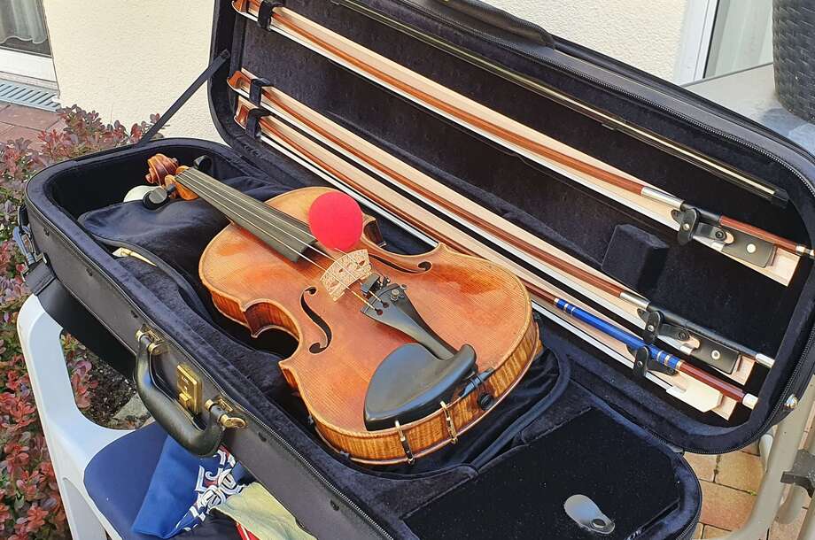 In einem aufgeklappten Geigenkasten liegt eine Violine mit einer roten Schaumstoffnase auf den Saiten.