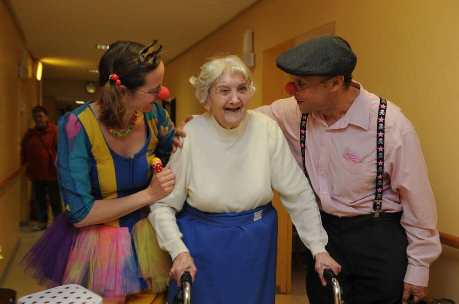 Zwei Clowns begleiten eine ältere Dame mit Rollator, die herzlich lacht