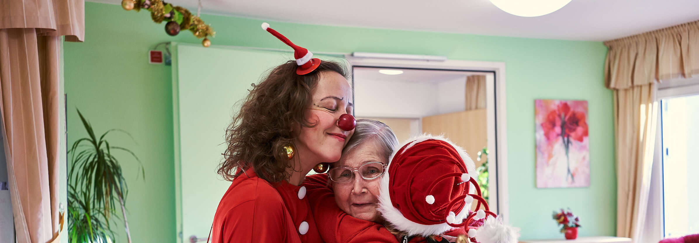 Zwei Clowns umarmen im Weinachts Kostüm eine ältere Frau 