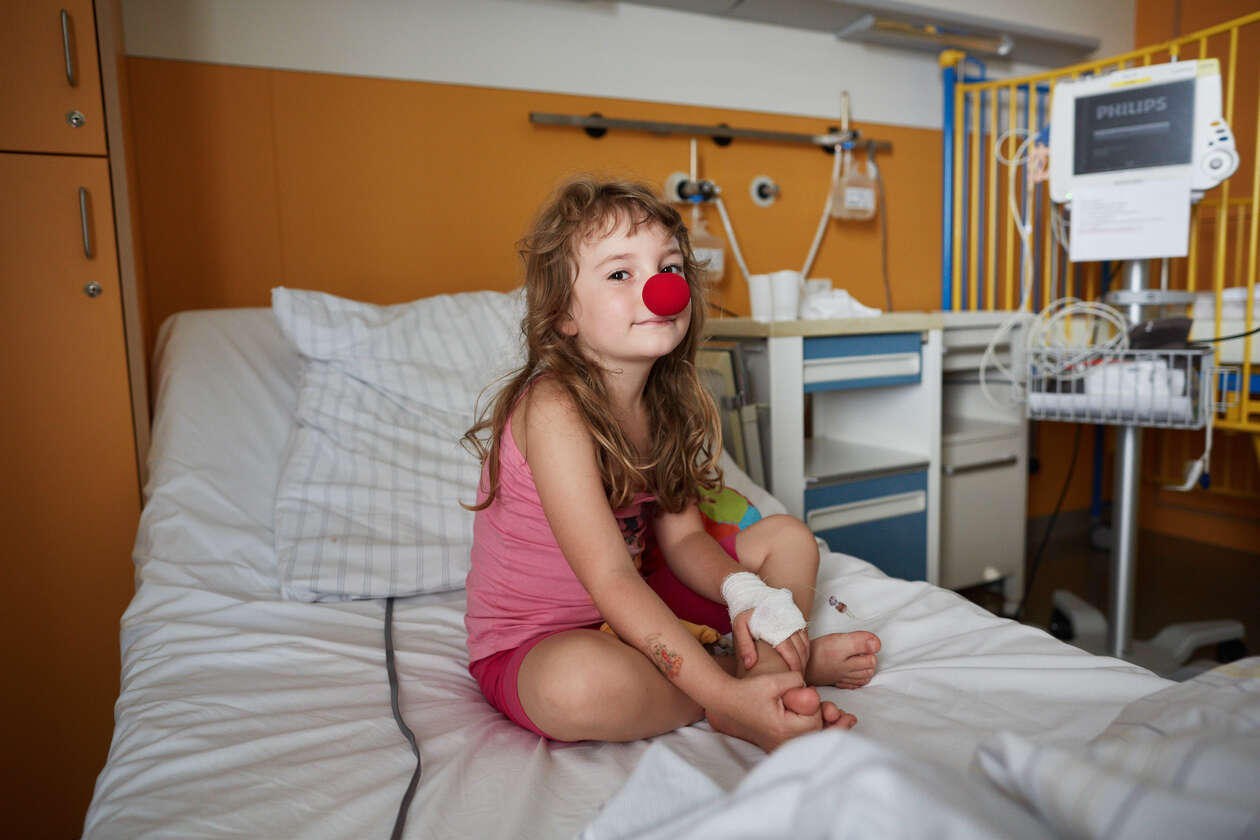 Ein Mädchen mit roter Schaumstoffnase sitzt im Krankenhausbett und lacht