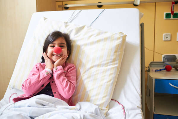 Ein Mädchen sitz in einem Krankenbett und hat eine rote Nase.