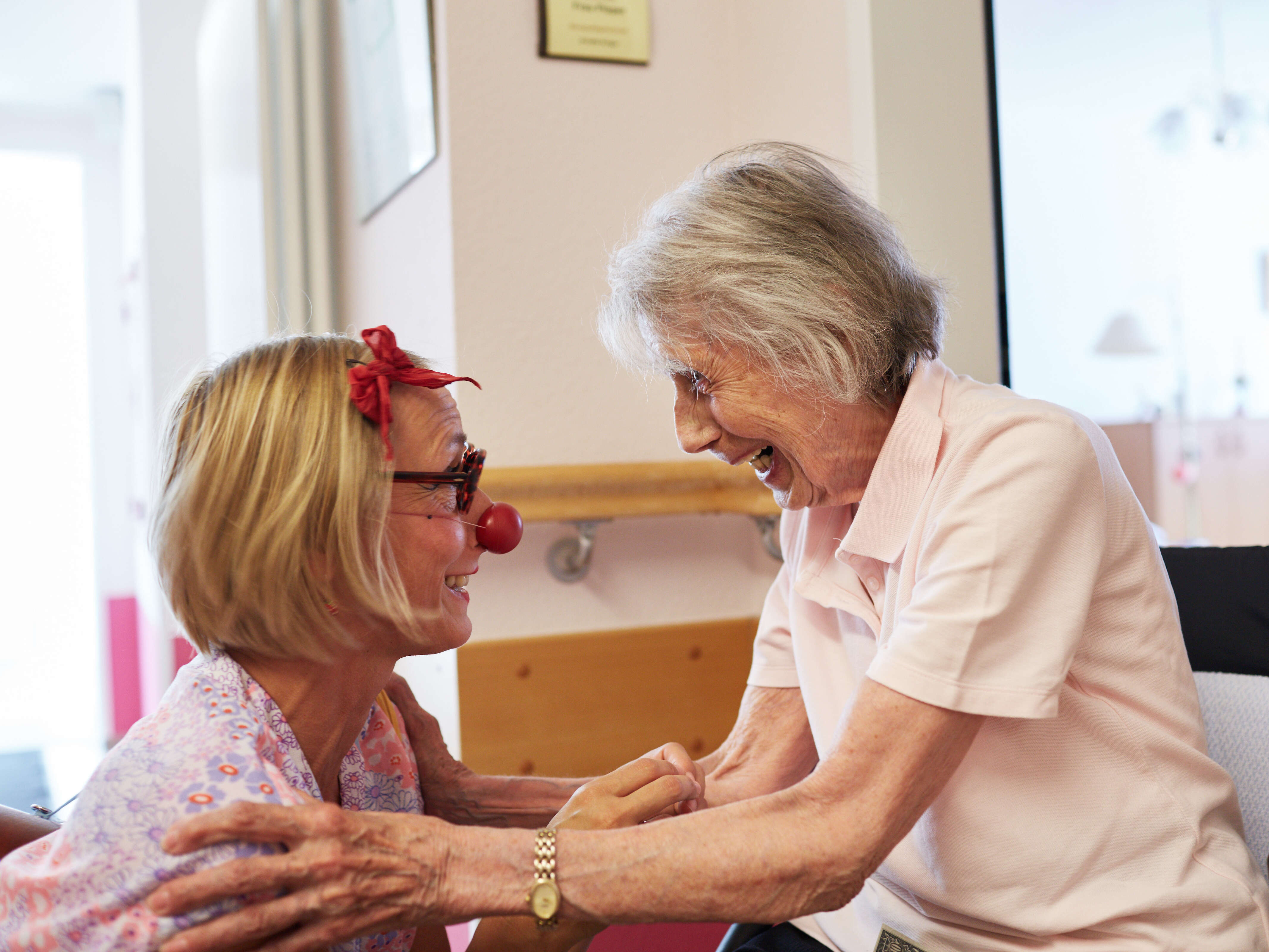 Eine Clownin kniet sich vor eine ältere lachende Dame hin