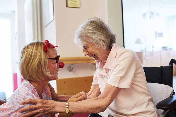 Eine Clownin kniet sich vor eine ältere lachende Dame hin