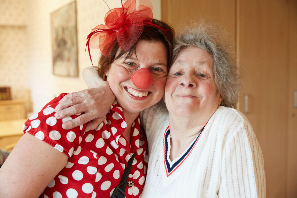 Ein Clown und Ein Seniore lacheln in dem Pflegeheim in die Kamara