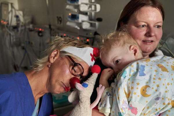 ROTE NASEN Clown Brischitt und ihre Kuscheltierratte Gustav kuschenl mit dem kleinen Luca, der am Herzen operiert werden soll. Seine Mutter schaut besorgt.