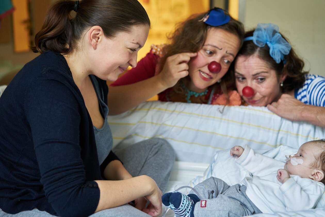 Clowns und die Mama schauen auf ein Baby mit Pflaster im Gesicht herab