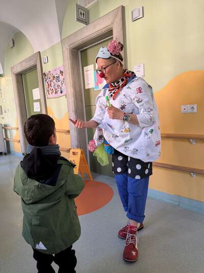 Ein Clown im OP-Kittel zeigt einem kleinen Jungen etwas im Krankenhausflur.