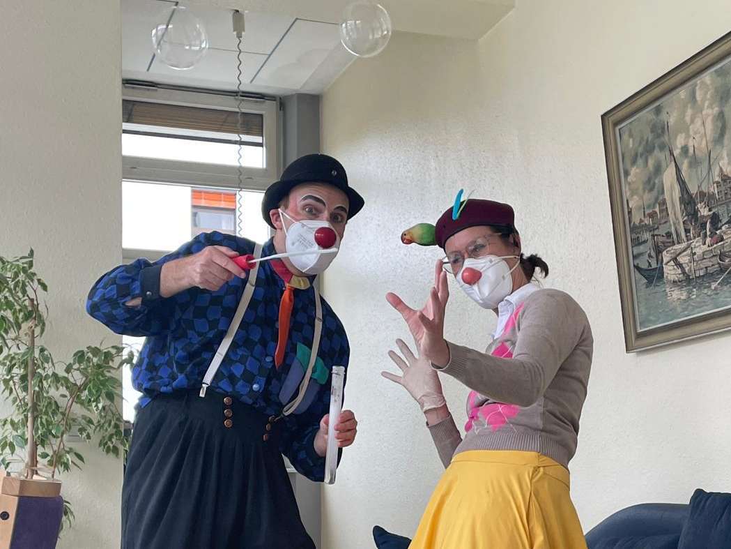 ROTE NASEN Clown Kleo alias Sandra Schüssler und Bobbly alias Jan Karpawitz schauen in die Kamera. Beide tragen bunte Anziehsachen, eine Clownsase und bunte Federn am Hut. ROTE NASEN Clownvisite bei Pflegebedürftigen im Karl-Olga-Haus in Friedrichshafen.
