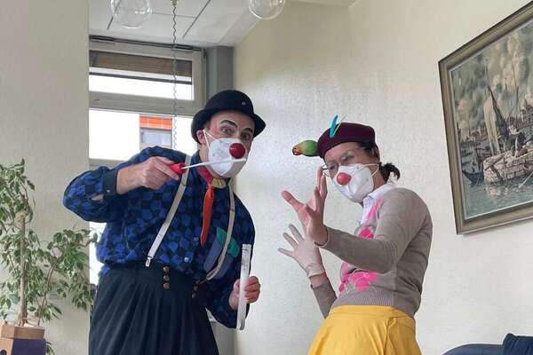 ROTE NASEN Clown Kleo alias Sandra Schüssler und Bobbly alias Jan Karpawitz schauen in die Kamera. Beide tragen bunte Anziehsachen, eine Clownsase und bunte Federn am Hut. ROTE NASEN Clownvisite bei Pflegebedürftigen im Karl-Olga-Haus in Friedrichshafen.