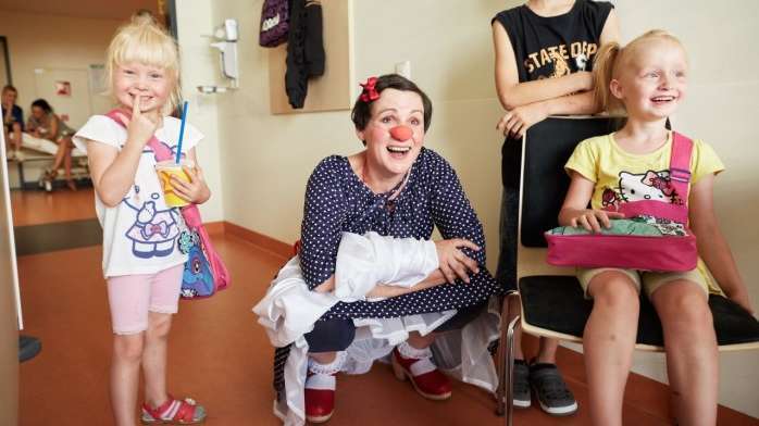 Die Clownin Nina hockt in der Mitte von drei jungen Mädchen und lacht