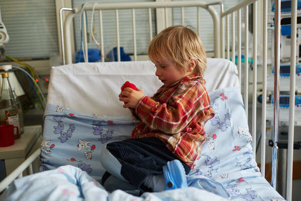Ein kleiner Junge spielt mit einer roten Nasen in seinem Krankenhausbett