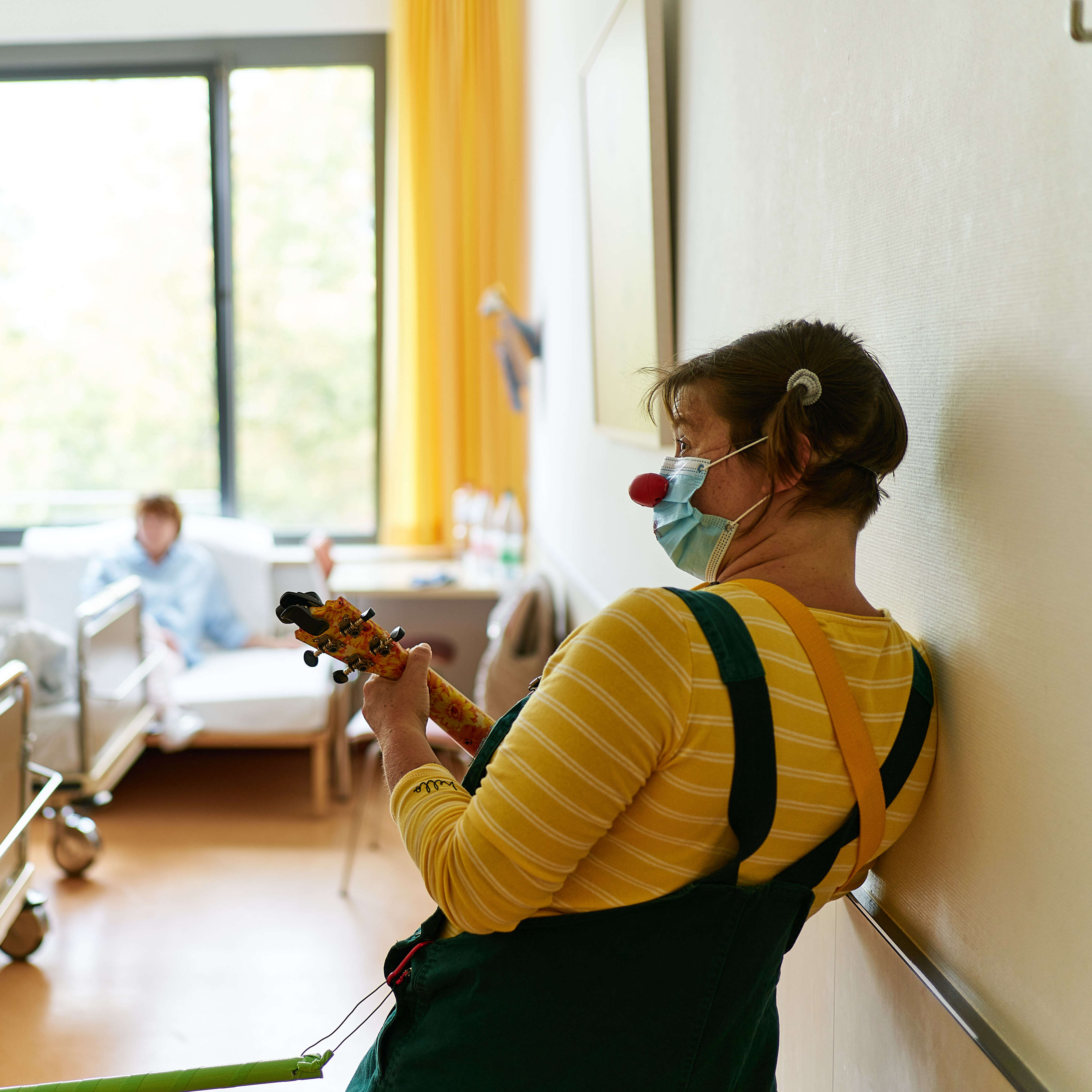 Gogo lehnt mit einer Ukulele an einer Wand im Krankenhaus