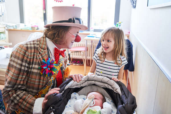 Ein Klinikclown besucht ein kleines lächeldes Mädchen in ihrem Krankenzimmer