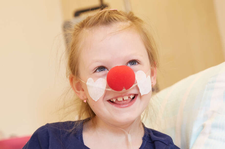 Ein Mädchen sitzt lächelt mit einer roten Nase in ihrem Krankenhausbett