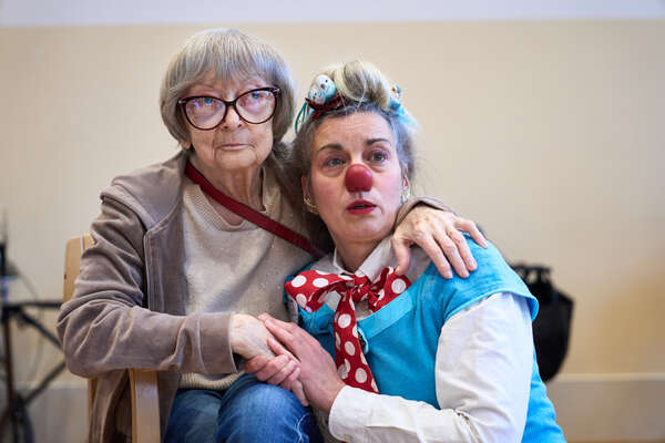 Ein Clown sitzt neben eine älteren Dame, die sie umarmt.