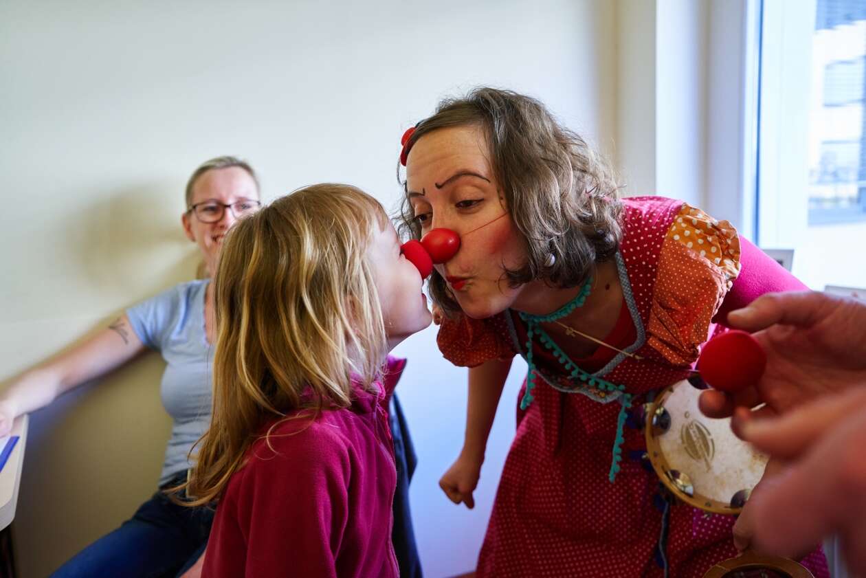 Ein kleines Mädchen berüht mit ihrer roten Clownsnase einen Klinikclown an der Nase 