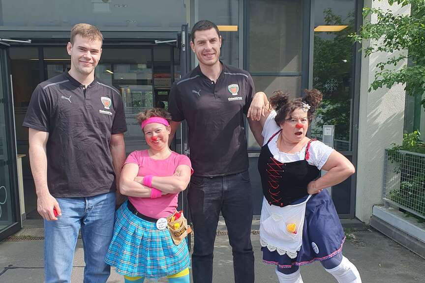 Zwei Handballspieler stehen mit zwei Clowns vor dem Eingang zur Notaufnahme des Klinikums Ernst von Bergmann.