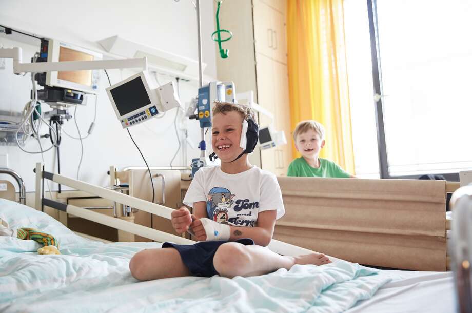 Ein Junge im Krankenhausbett sitzend lacht herzlich. Nicht im Bild zu sehen ist der ROTE NASEN Klinikclown.