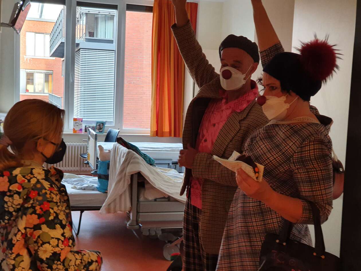 2 Clowns stehen im Zimmer einer Patientin und raten ein Ratespiel mit Kuchen in der Hand