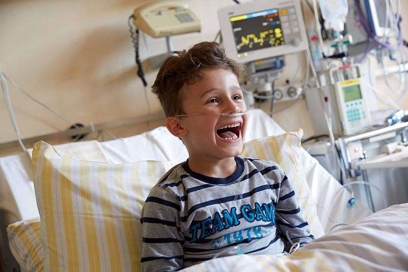 Ein Junge schaut von seinem Krankenbett aus zu und lacht über Klinikclowns