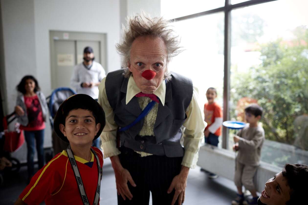Ein Junge aus einer Fluchtlingsunterkunft grinst in die Kamara, während ein Clown daneben schmunzelt 