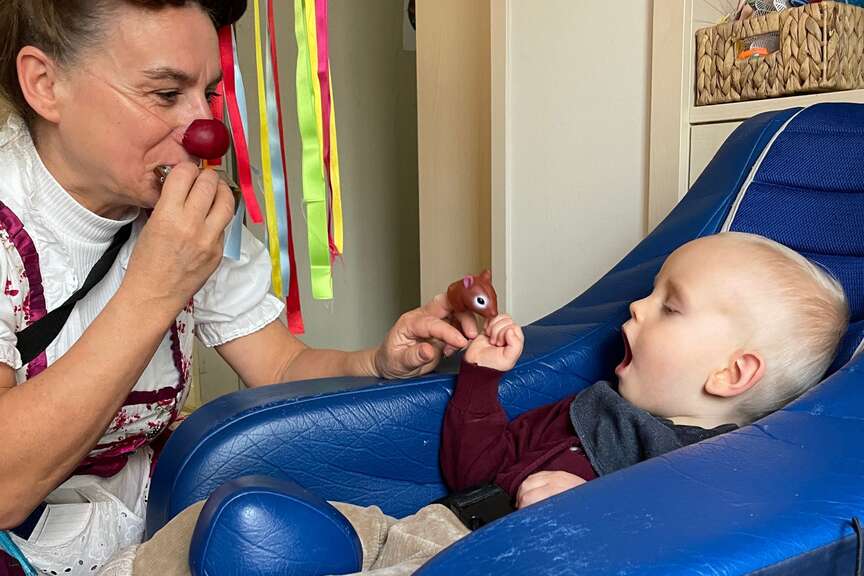 Ein Clown spielt einem kleinem Jungen auf einer Mundharmonika etwas vor. 