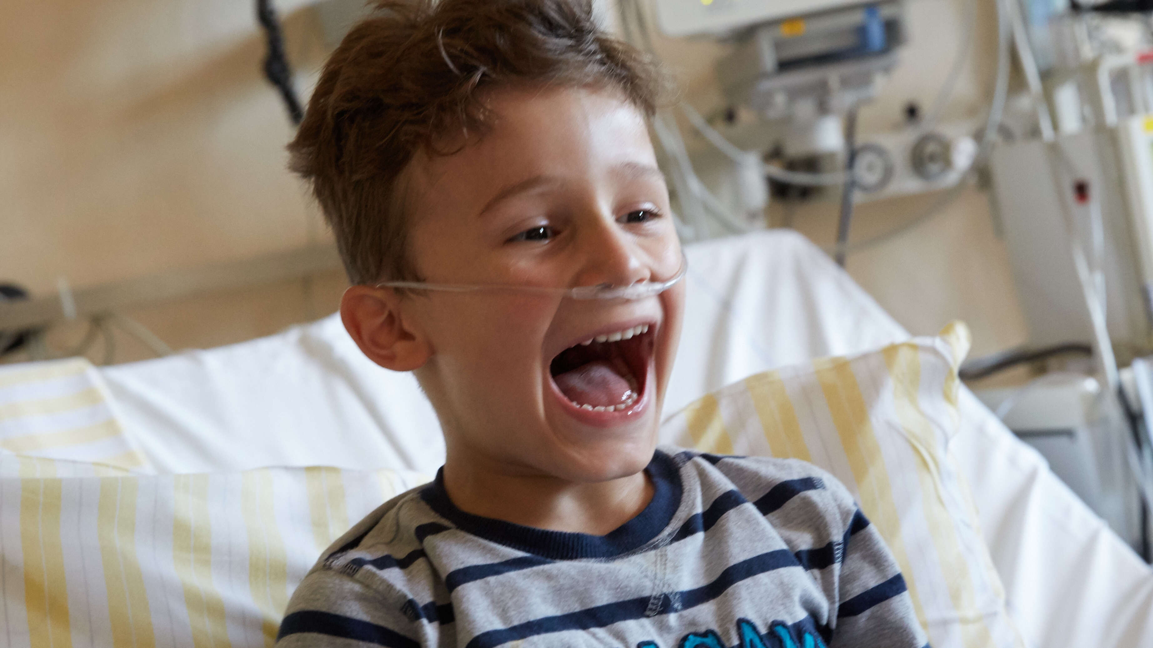 Tom, ein krebskranker Junge, liegt während einer Clownvisite lachend im Bett 