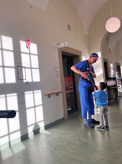 Ein Clown steht mit einem kleinen Jungen im Krankenhausflur und sie schauen sich beide an.