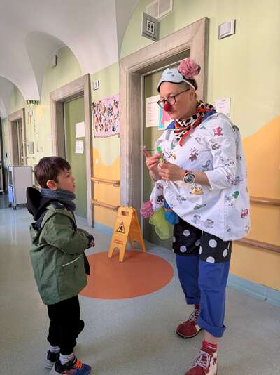 Ein Clown im OP-Kittel zeigt einem kleinen Jungen einen Zaubertrick.