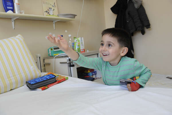 Ein kleiner Junge mit einem Verband am Arm streckt seine Hand aus und lächelt.