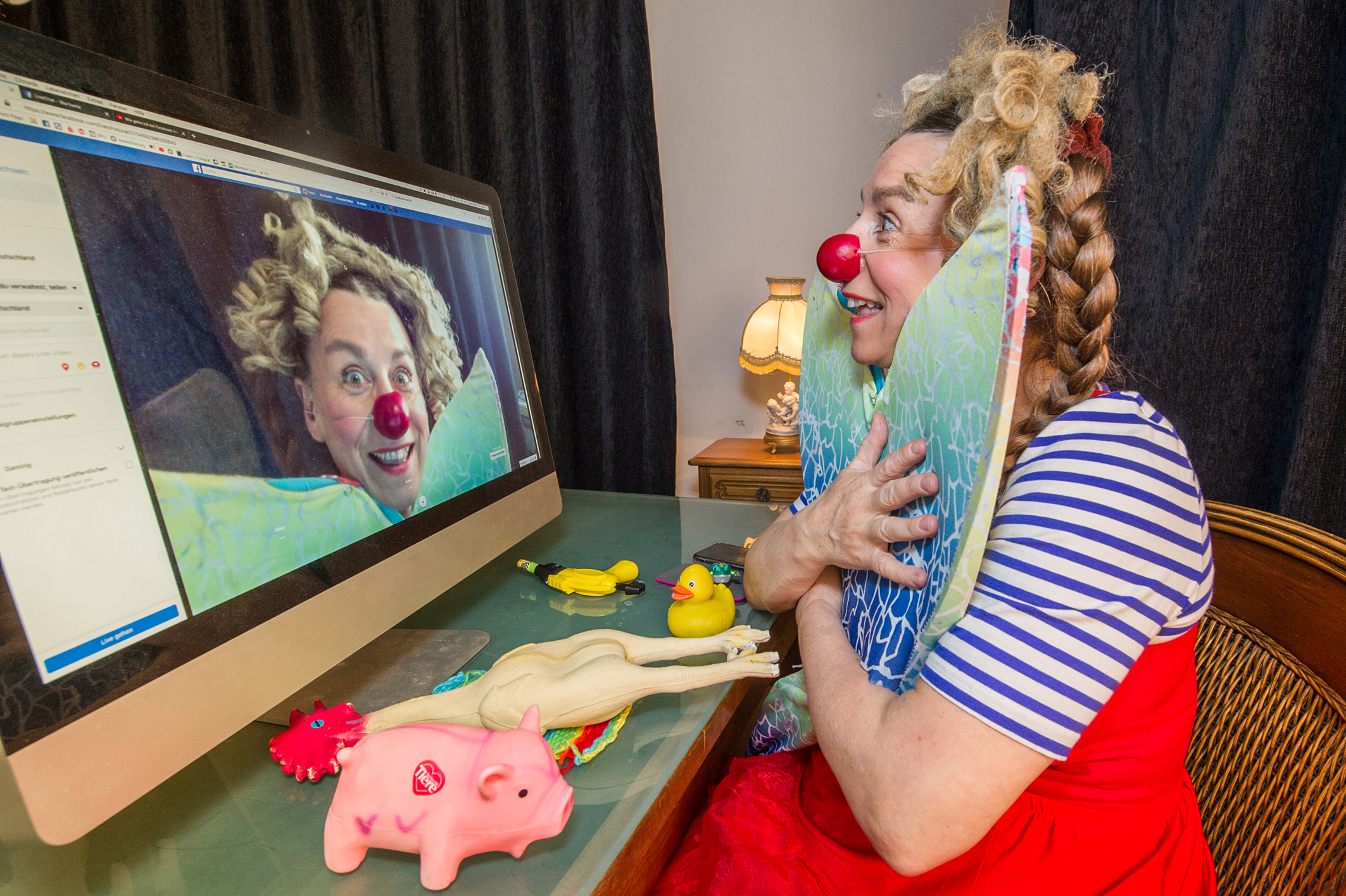 Clown Antonia sitzt mit zwei Flügeln in der Hand vor einem Computer und schaut auf den Display.