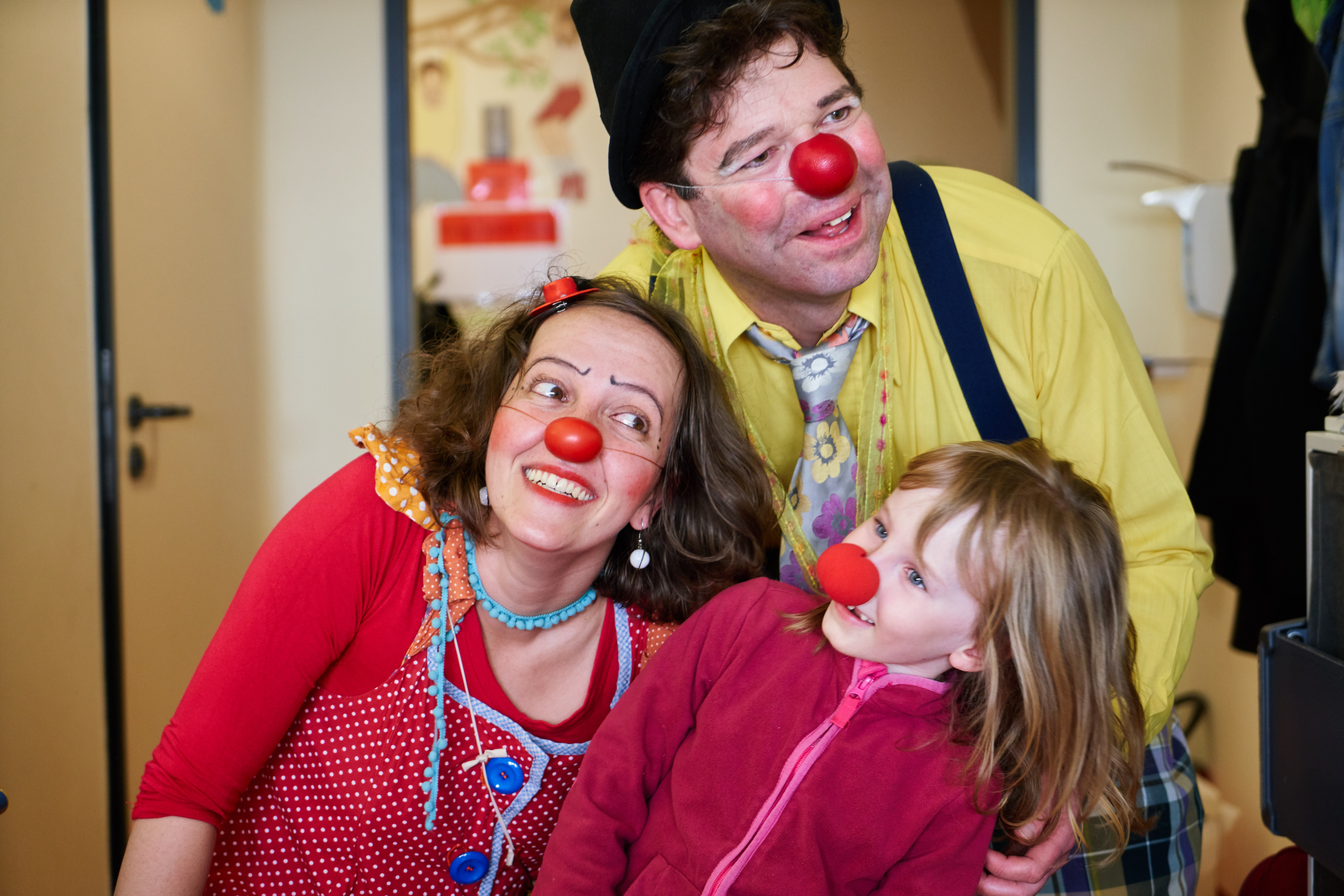 Zwei Klinikclowns spielen mit einem Mädchen was auch eine rote Nase bekommen hat