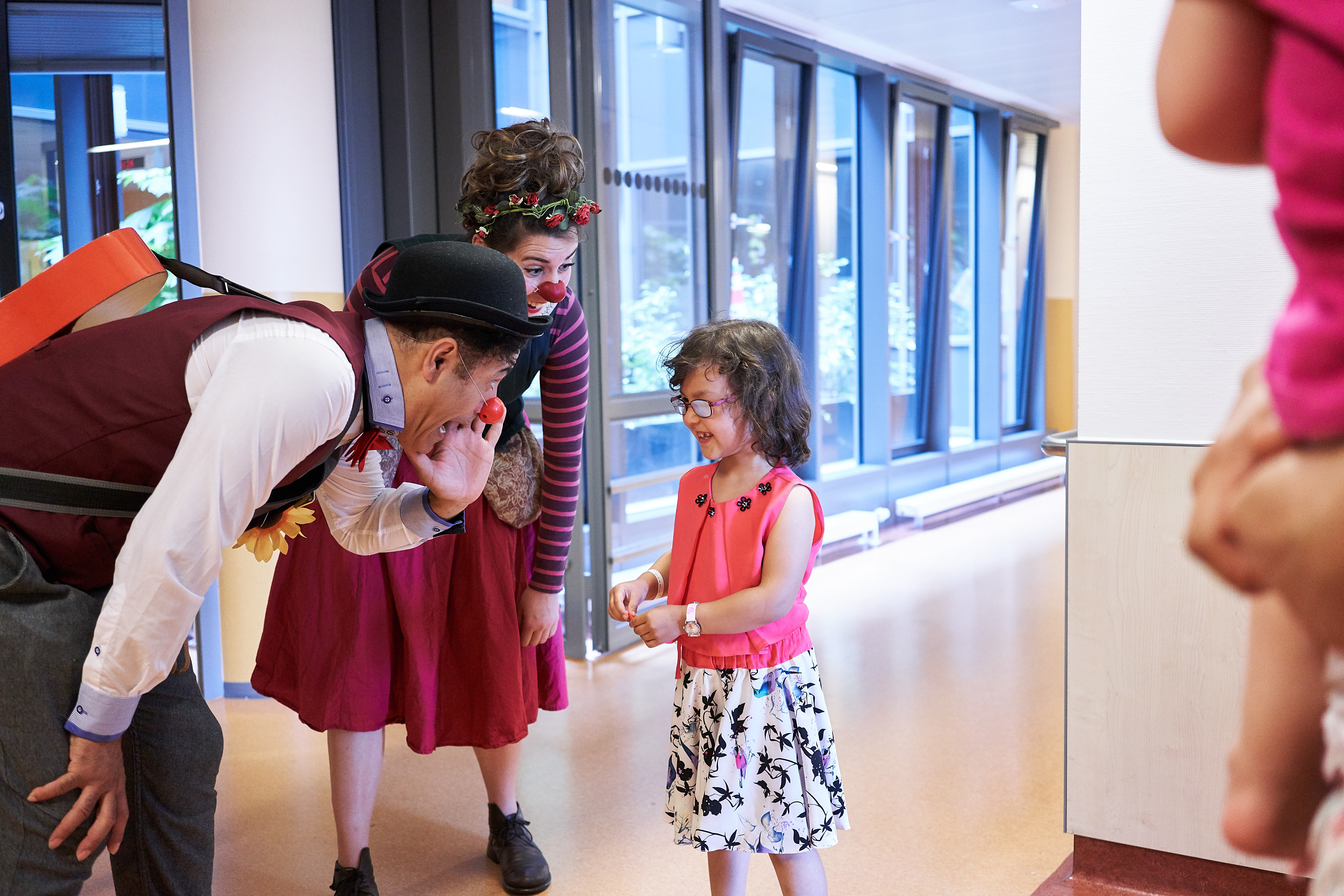 Klinikclowns sprechen mit einem kleinem Mädchen auf den Krankenhaus Fluren 