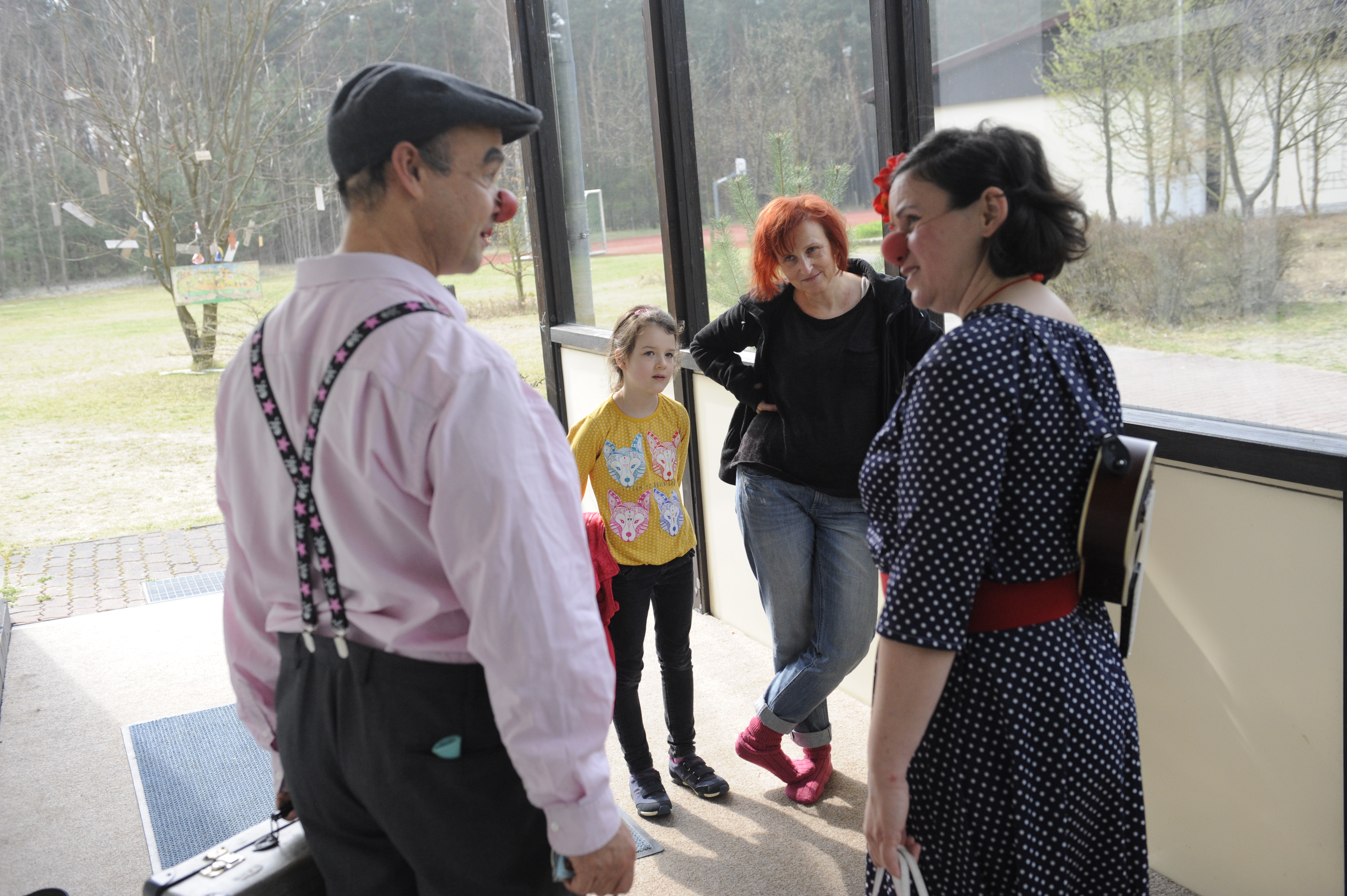 Zwei Klinikclowns sprechen miteinander und eine Mutter mit ihrer kleiner Tochter schauen zu 