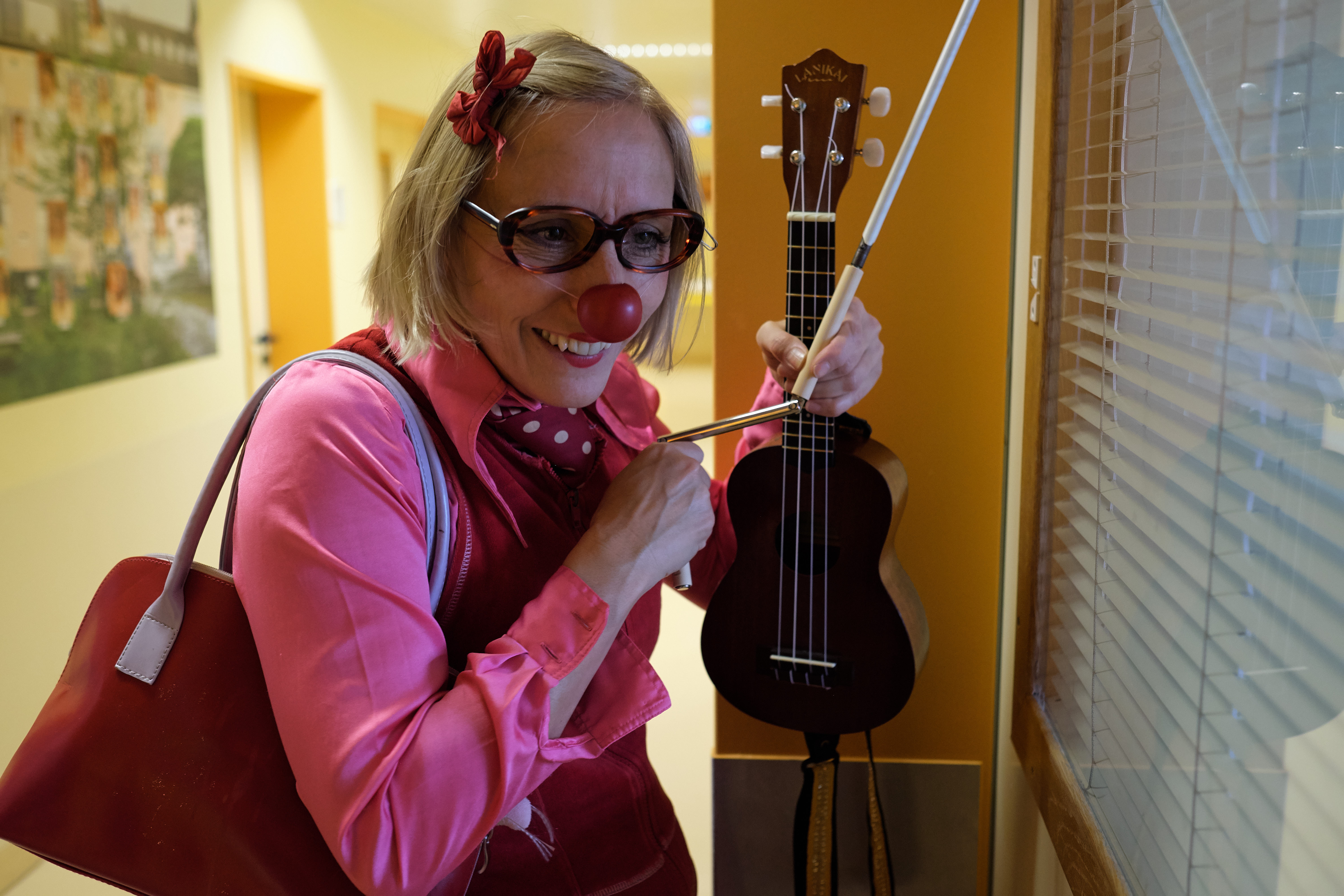 Ein Clown hält eine Ukulele in der Hand und steh vor einem Krankenzimmer