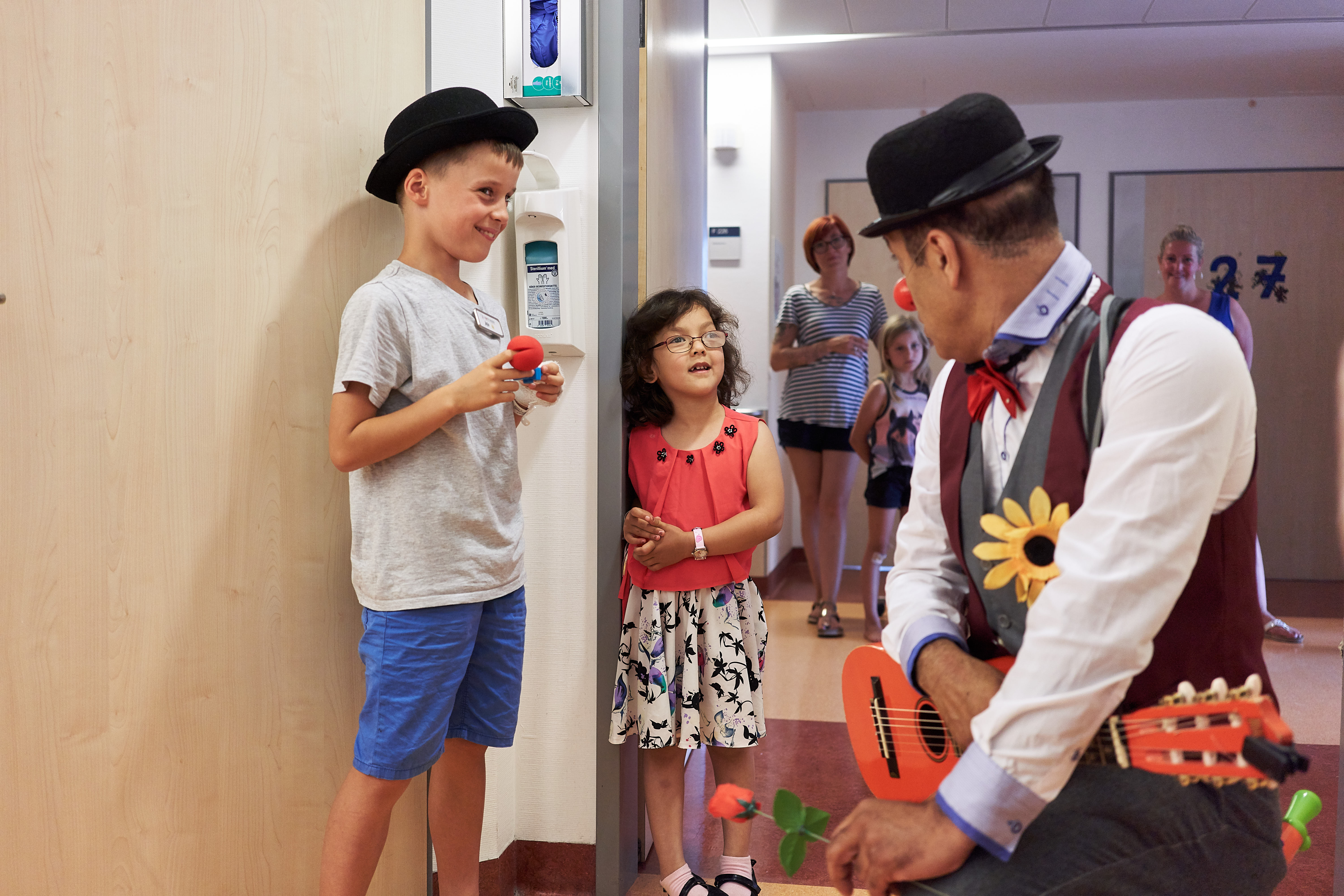 Clown spricht mit einem Mädchen und einem Jungen in einem Krankenhaus