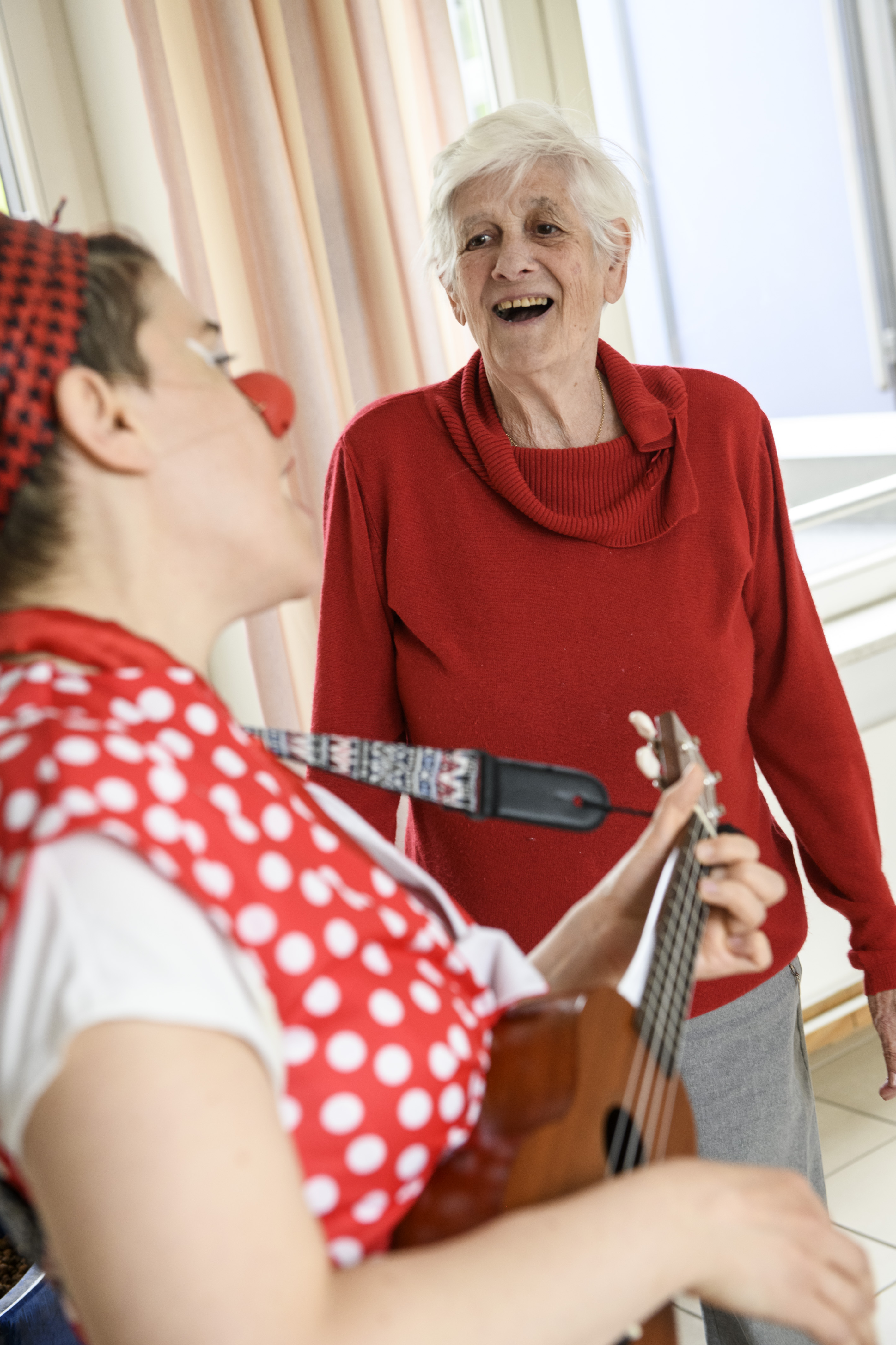 Clownin trällerd einer alten Dame in einer Pflege Einrichtung ein Lied auf ihrer Ukulele vor 